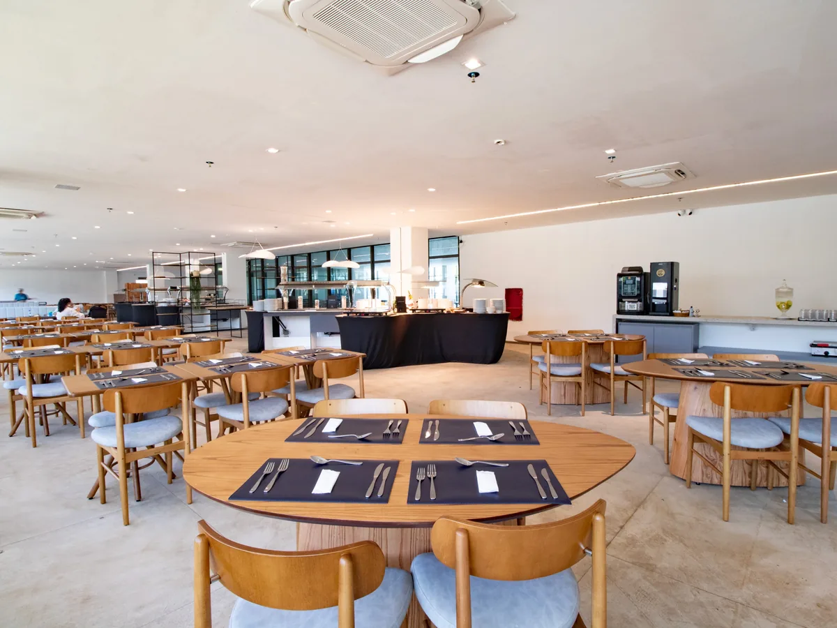 Salão do restaurante Tanino, do Maceió Mar Resort, com mesas de madeira postas e o bufê ao fundo