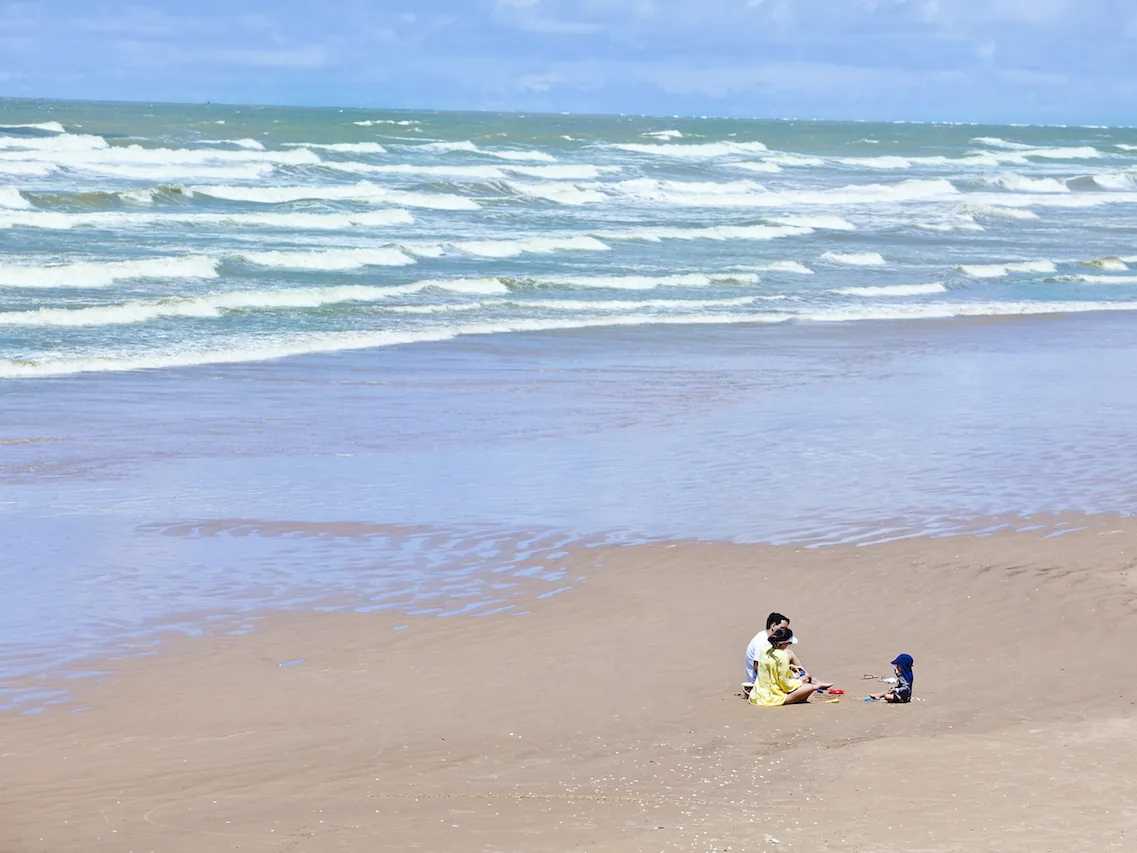 Praia larga e vazia em frente ao Makai Resort, com uma família brincando na areia