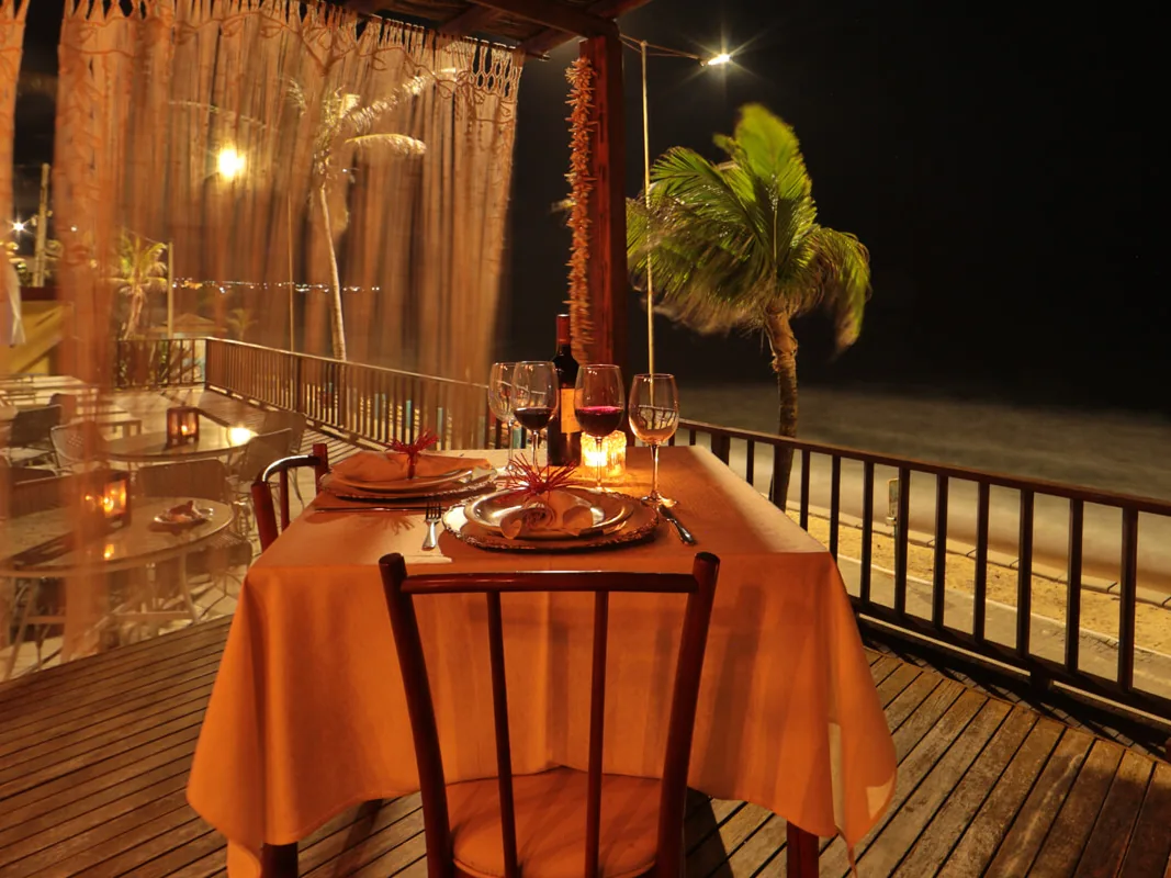 Mesa para dois à luz de velas no deque do Manary Praia Hotel, à noite, com a praia ao lado