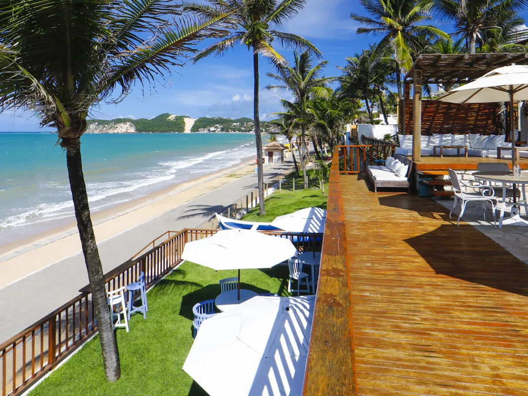 Deque de madeira do Manary Praia Hotel à beira-mar, com guarda-sóis, coqueiros e a praia de Ponta Negra ao lado