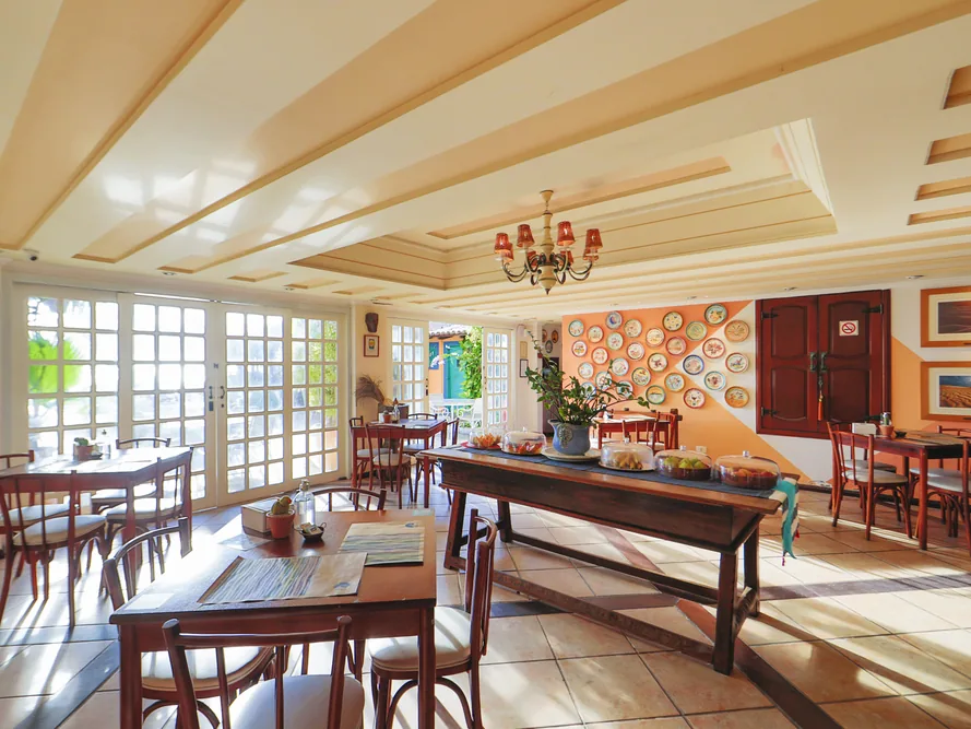 Salão do restaurante do Manary Praia Hotel com mesas de madeira, lustre e pratos decorativos na parede