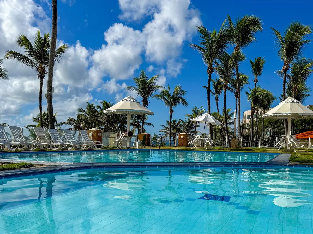 Piscina do Marsol Beach Resort cercada de coqueiros, com espreguiçadeiras e guarda-sóis brancos