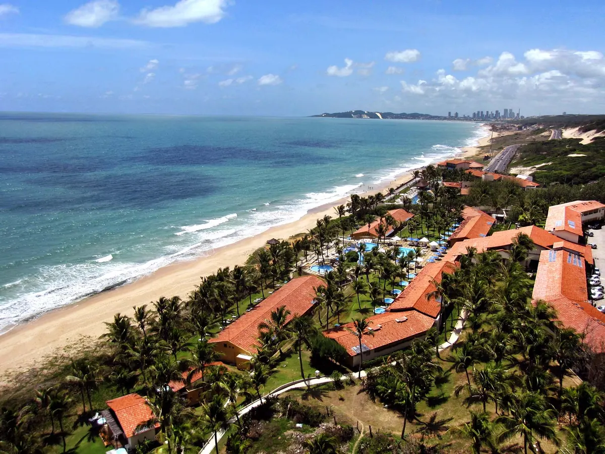 O Marsol Beach Resort visto do alto, com os telhados vermelhos entre coqueiros, as piscinas e a praia, e a cidade ao fundo