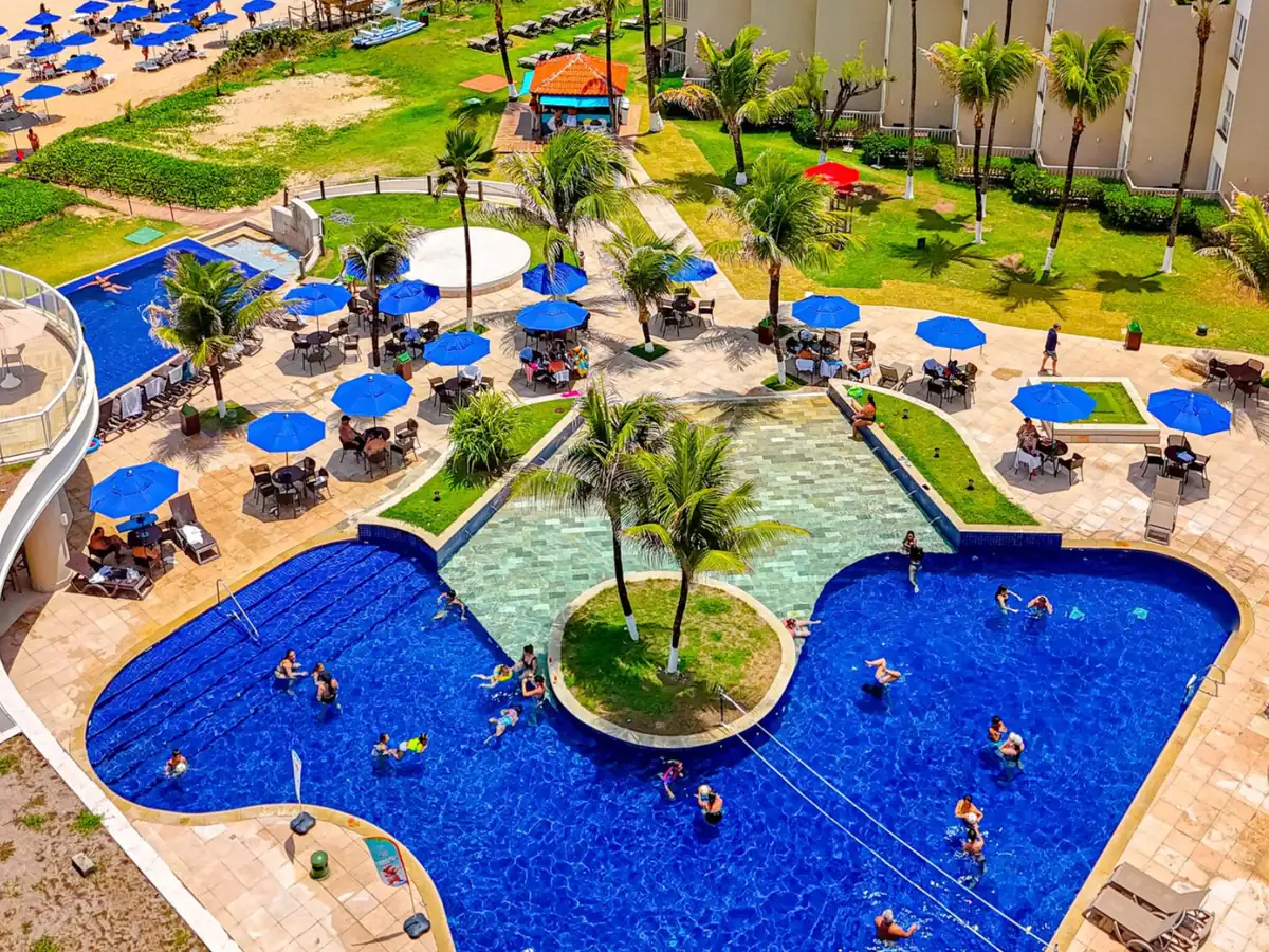 Piscina do Marupiara Resort vista do alto, com guarda-sóis azuis e os prédios ao redor