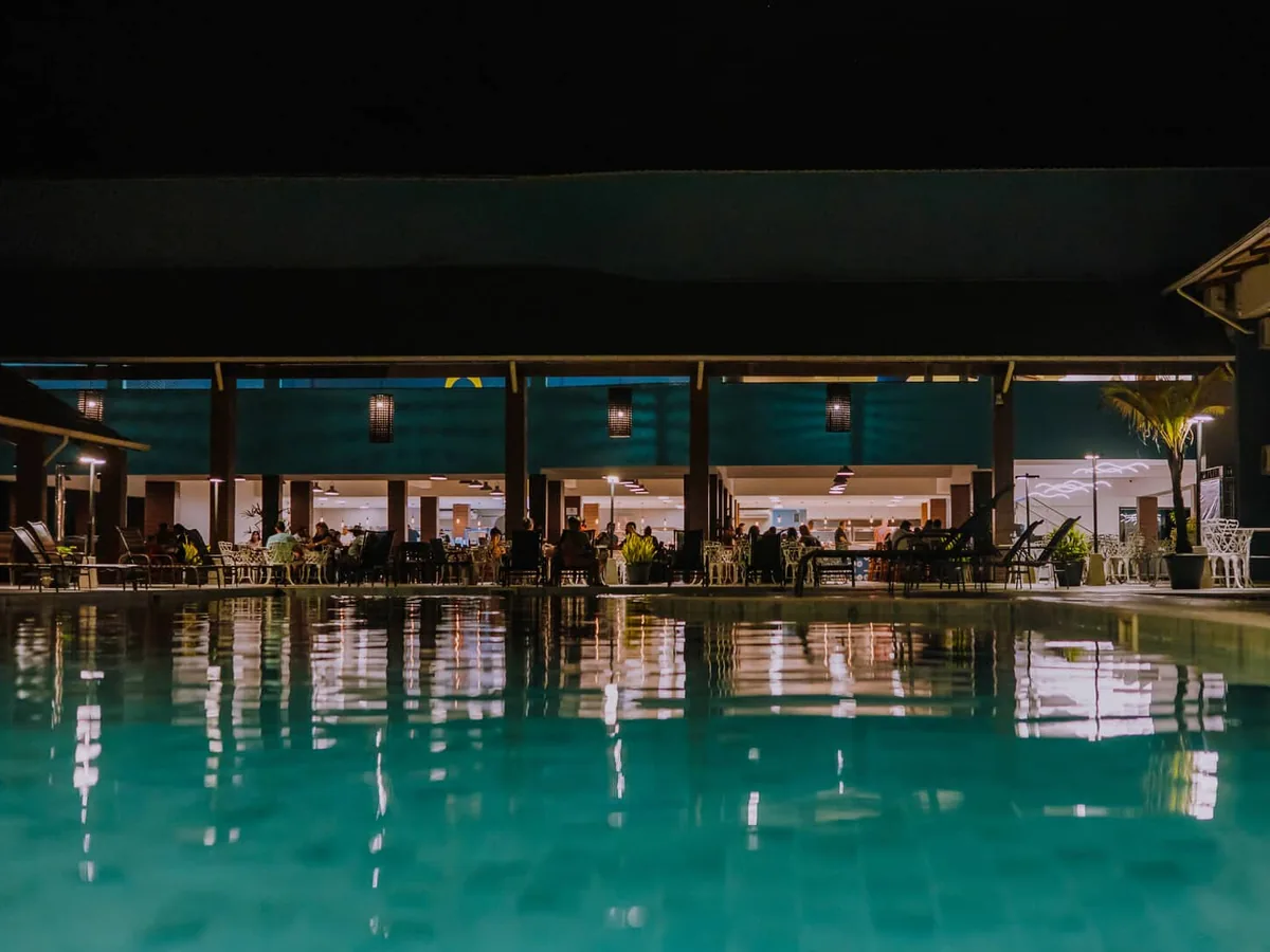 Piscina do Nauticomar Resort iluminada à noite, com o restaurante aberto ao fundo