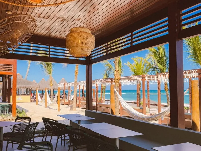 Mesas de um restaurante do Ocaporã Hotel, com luminárias de palha e vista para as redes e o mar