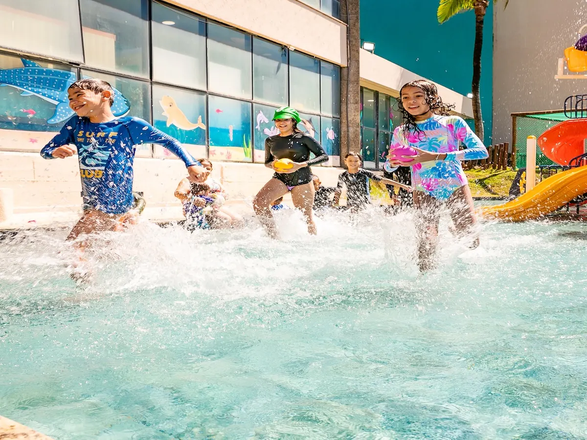 Crianças correndo na piscina infantil do Ocean Palace, com escorregadores coloridos ao fundo