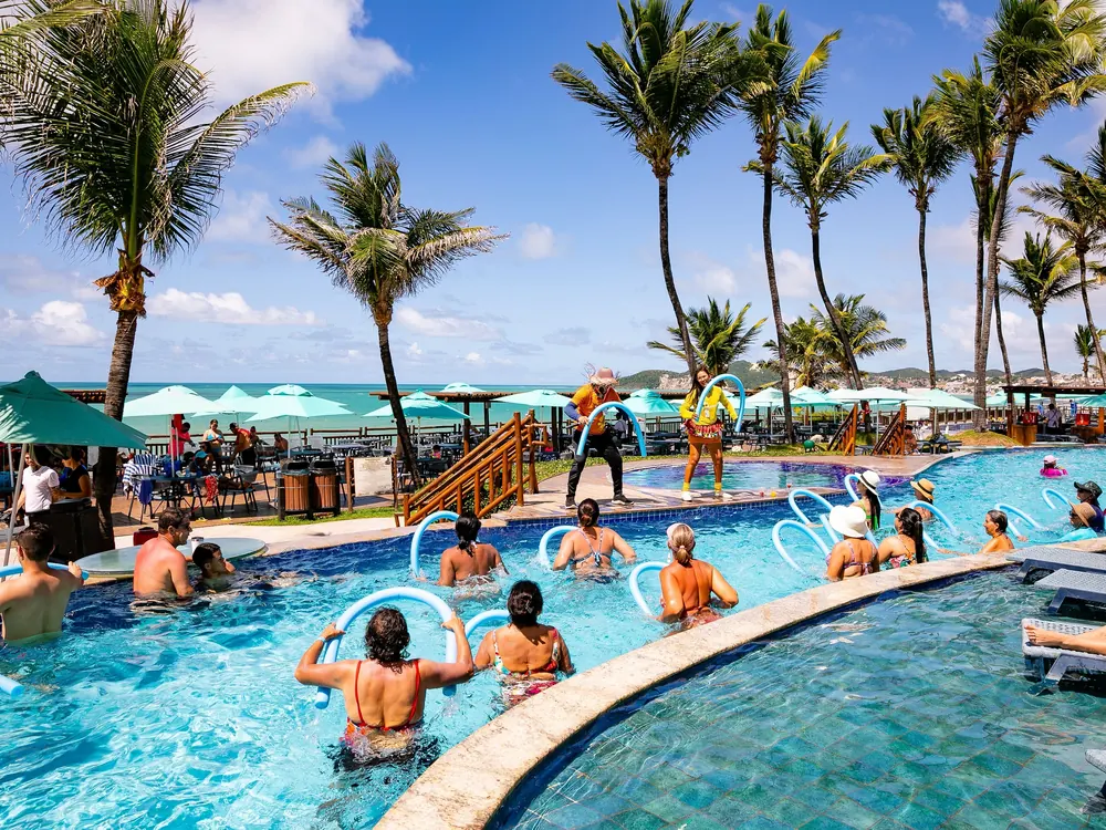 Aula de hidroginástica na piscina do Ocean Palace, com monitores e coqueiros ao fundo