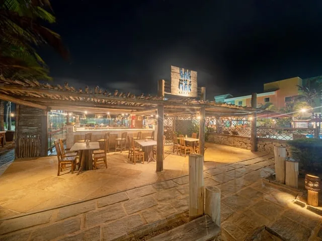 Bar do Mar do Oceani Beach Park iluminado à noite, com mesas no deque