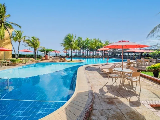 Piscina do Oceani Beach Park com guarda-sóis vermelhos e coqueiros, junto à praia