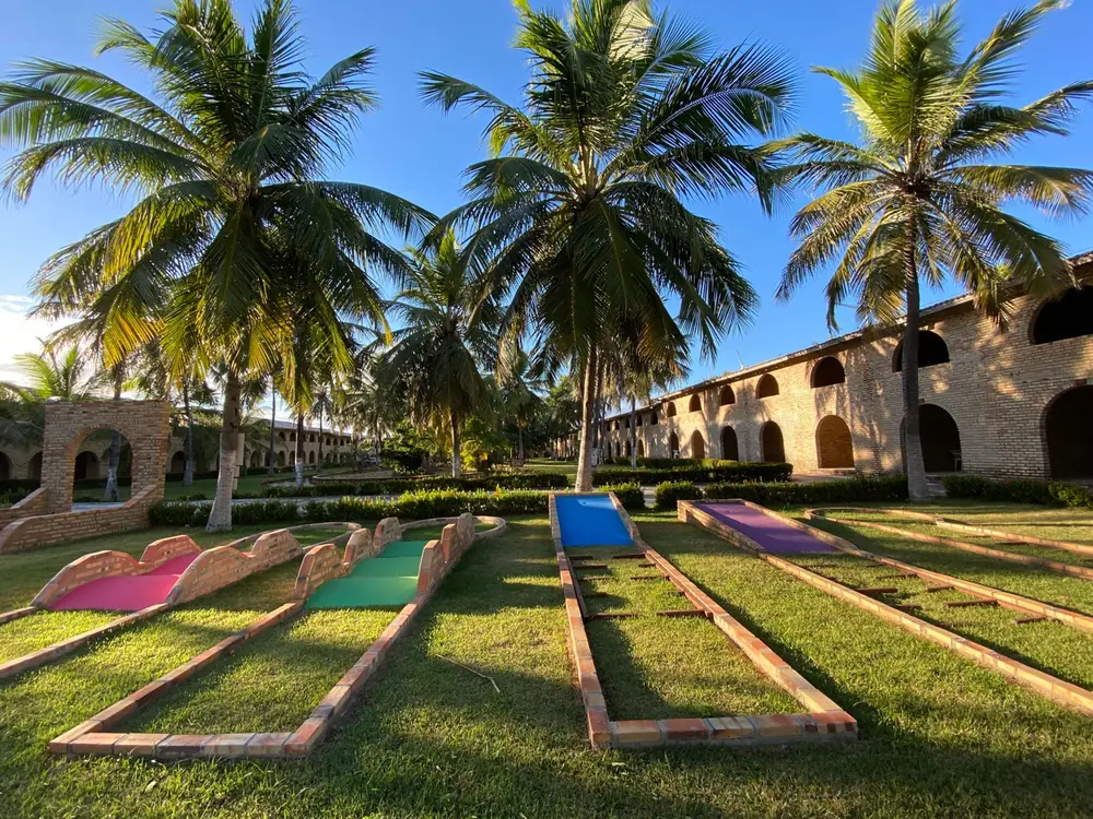 Pistas coloridas de minigolfe no gramado do Hotel Parque das Fontes, entre coqueiros e prédios de tijolo com arcos