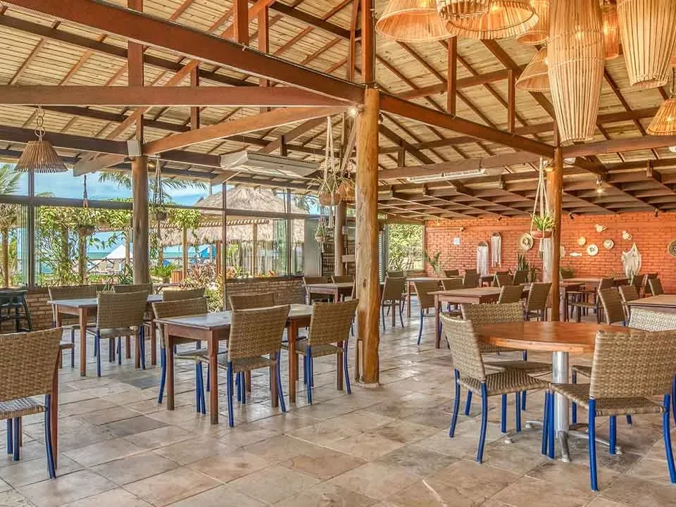 Restaurante do Salinas Maceió com mesas de madeira, luminárias de palha e vista para o mar