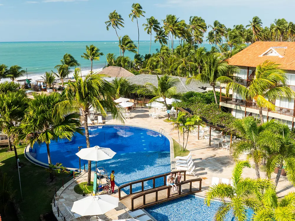 Piscina do Salinas Maceió vista do alto, com a ponte de madeira, os coqueiros e o mar de Ipioca ao fundo