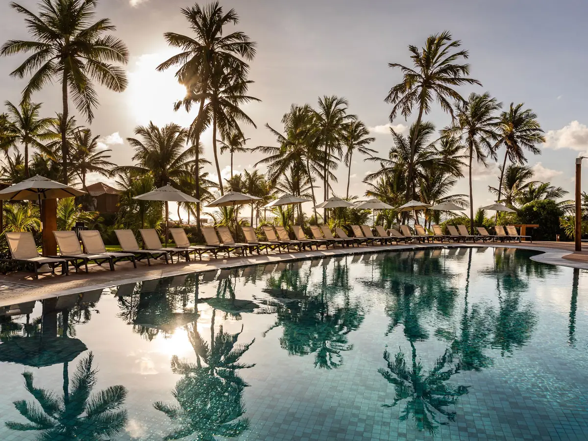 Piscina do Sauípe Sol Grand Premium ao entardecer, com coqueiros refletidos na água e espreguiçadeiras em fila