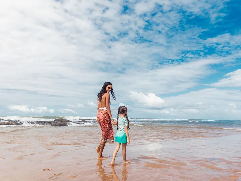 Mãe e filha caminhando de mãos dadas na beira do mar da Costa do Sauípe