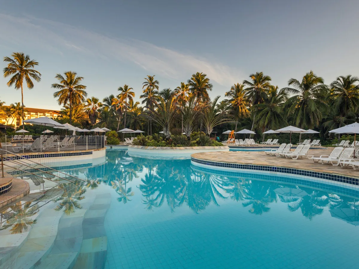 Piscina do Sauípe Terra Resort ao entardecer, com coqueiros refletidos na água e espreguiçadeiras em volta