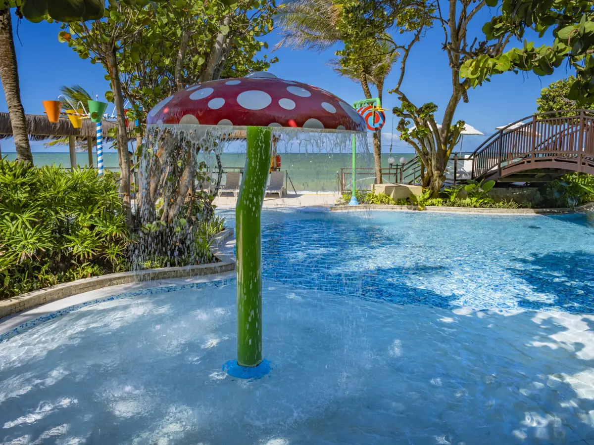 Piscina infantil do SERHS Natal com fonte em forma de cogumelo, ponte de madeira e o mar ao fundo