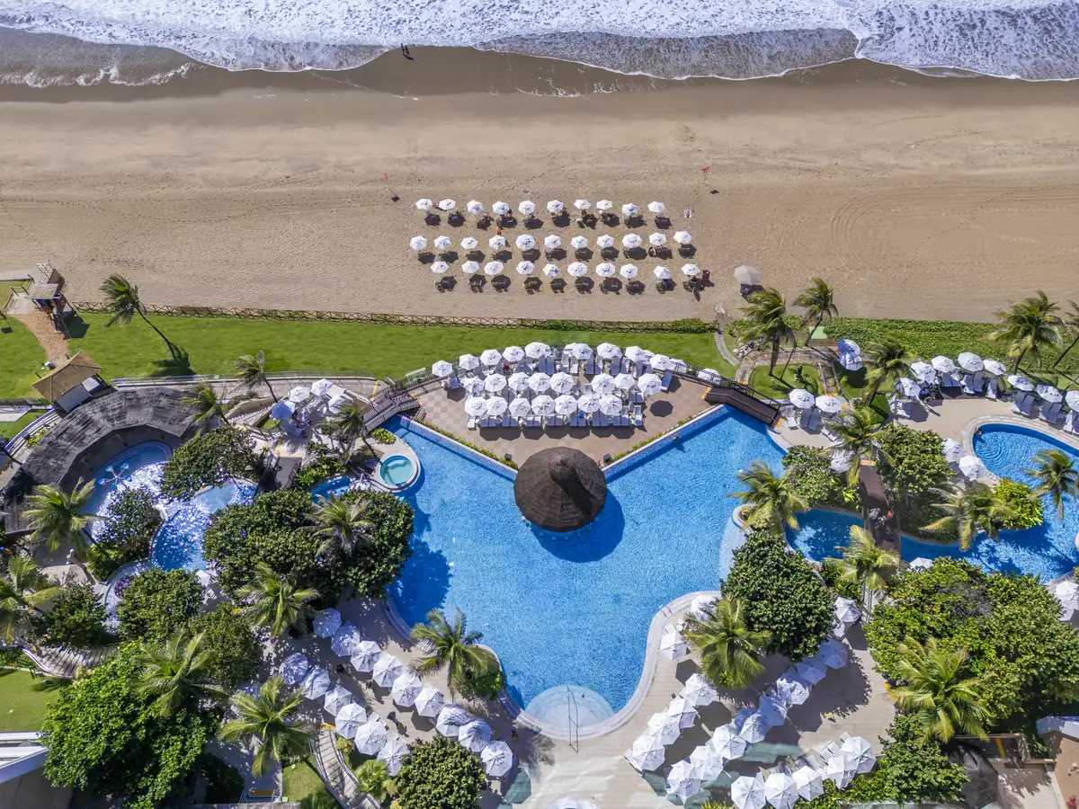 Piscina principal do SERHS Natal vista de cima, com o bar de palha, guarda-sóis brancos e a praia em frente