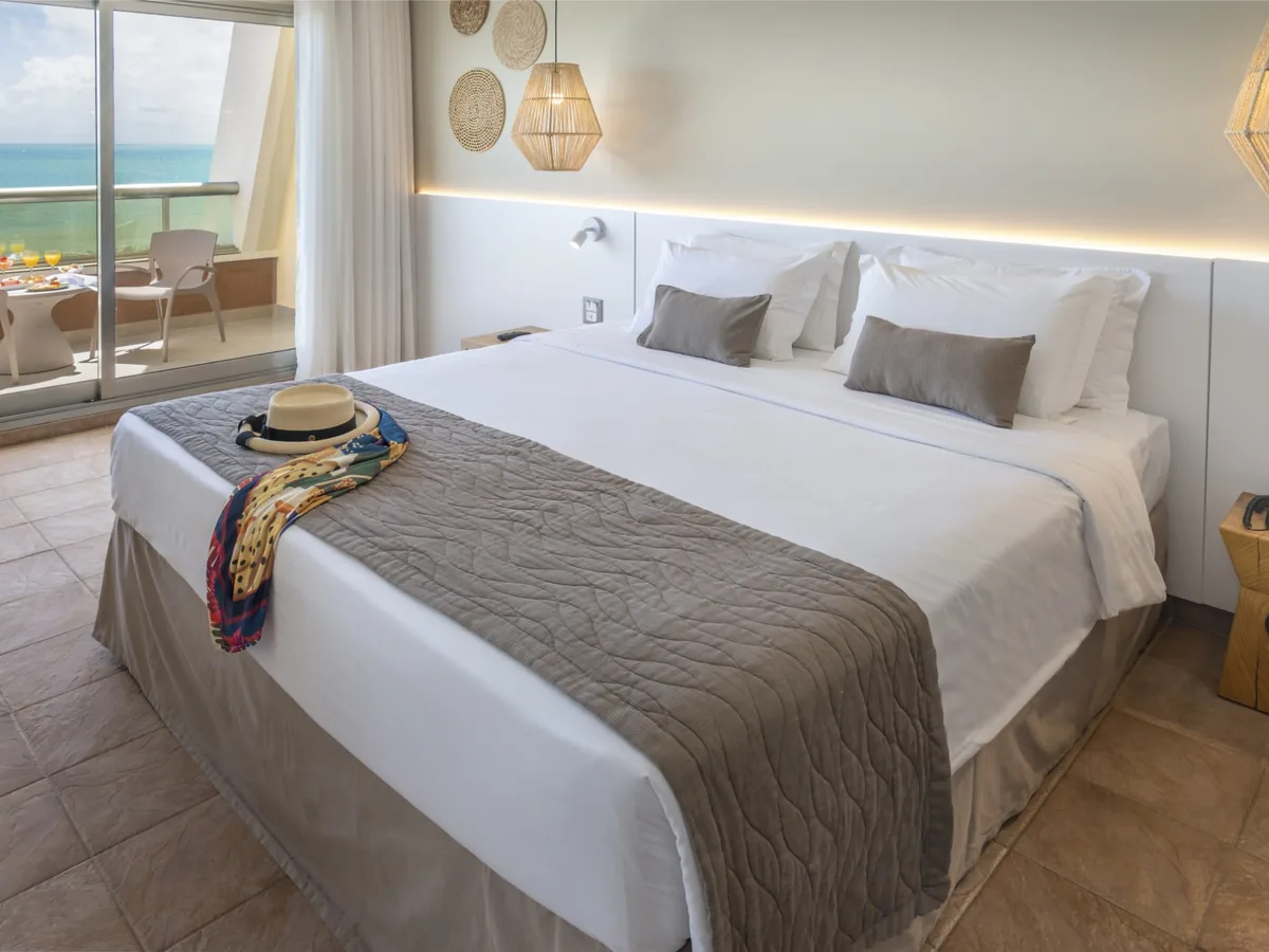 Quarto do SERHS Natal com cama de casal e porta de vidro para a varanda com vista para o mar