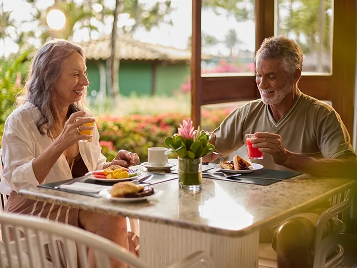 Casal tomando café da manhã numa varanda do Transamerica Comandatuba, com o jardim florido ao fundo