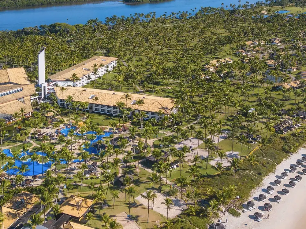 Transamerica Comandatuba visto do alto, com o canal ao fundo, as piscinas entre os coqueiros e os guarda-sóis na praia