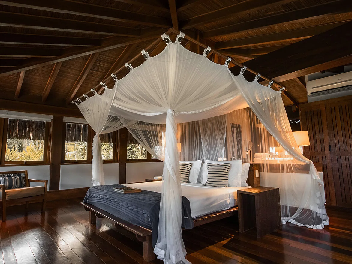 Quarto do Bangalô Praia do Txai, com cama de dossel e mosquiteiro, teto de madeira e janelas para o jardim