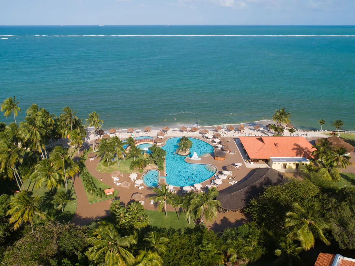 Piscina do Vila Galé Cabo vista do alto, cercada de coqueiros, com a praia ao lado