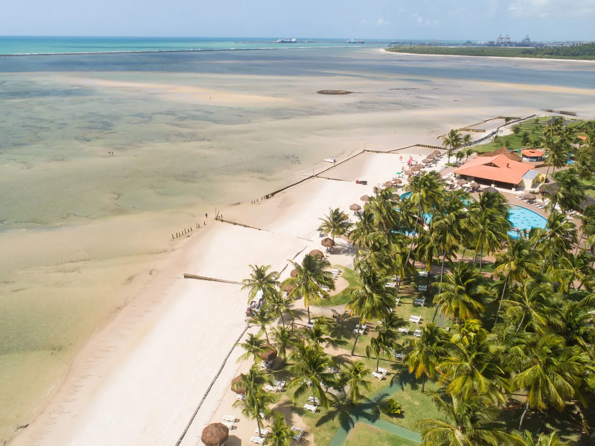 Praia de areia clara com coqueiros e o mar de águas rasas perto do Vila Galé Cabo