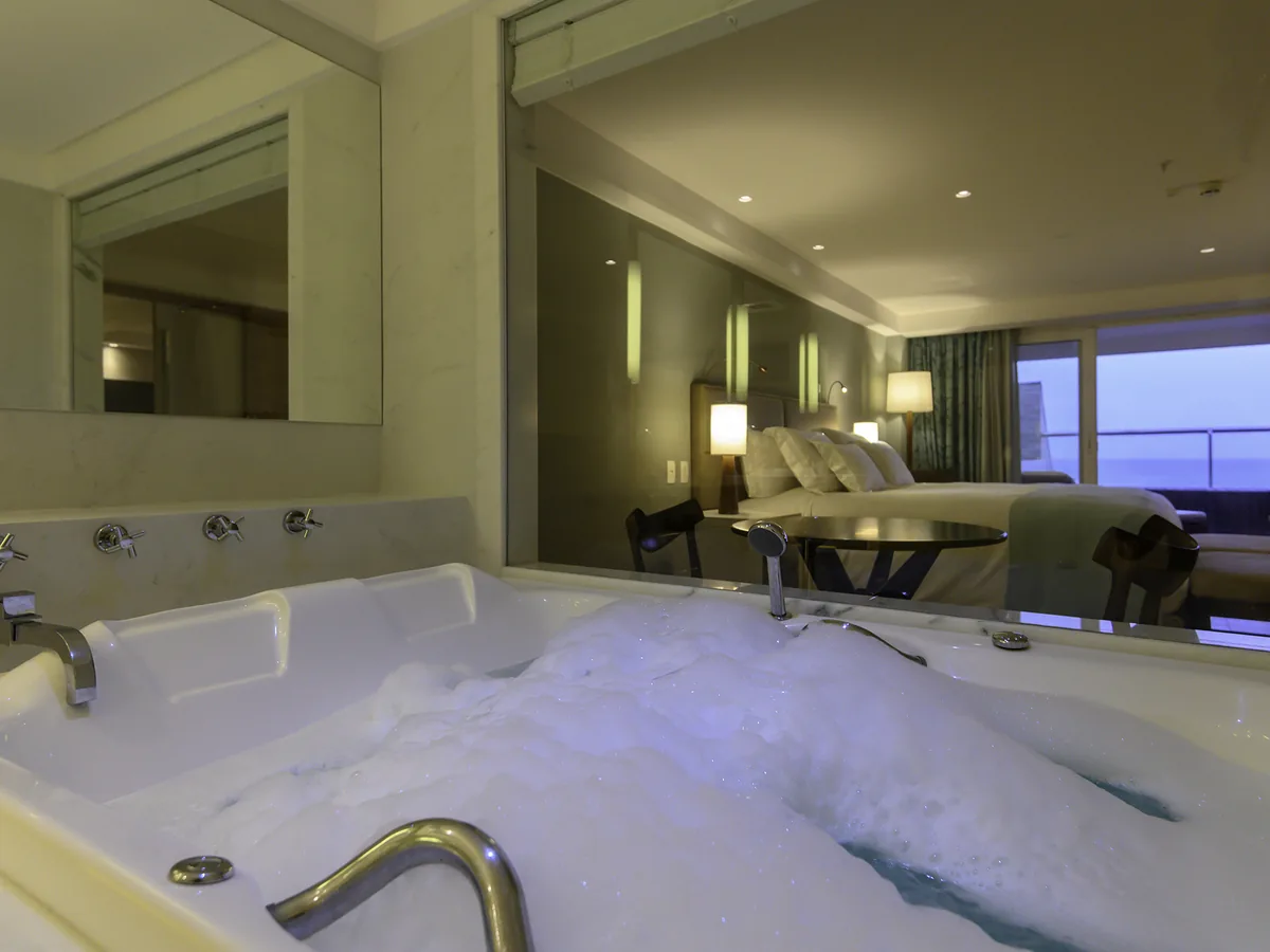 Banheira dupla de hidromassagem com espuma no Apartamento Luxury do Vogal, com o quarto e o mar ao fundo