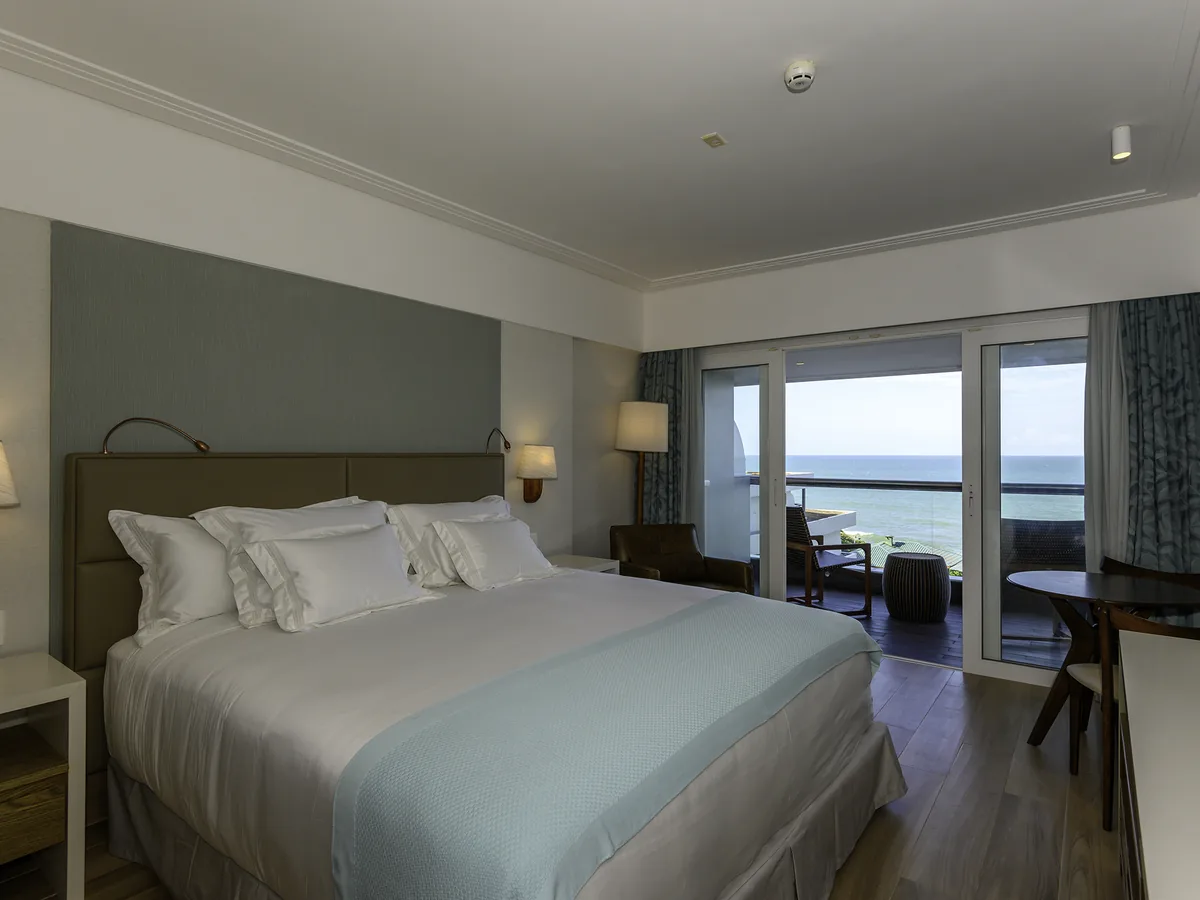 Apartamento Luxury do Vogal Luxury Beach Hotel com cama de casal e porta de vidro aberta para a varanda e o mar