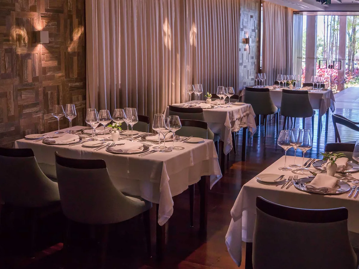 Salão de restaurante do Vogal com mesas de toalha branca, taças de cristal e cortinas claras