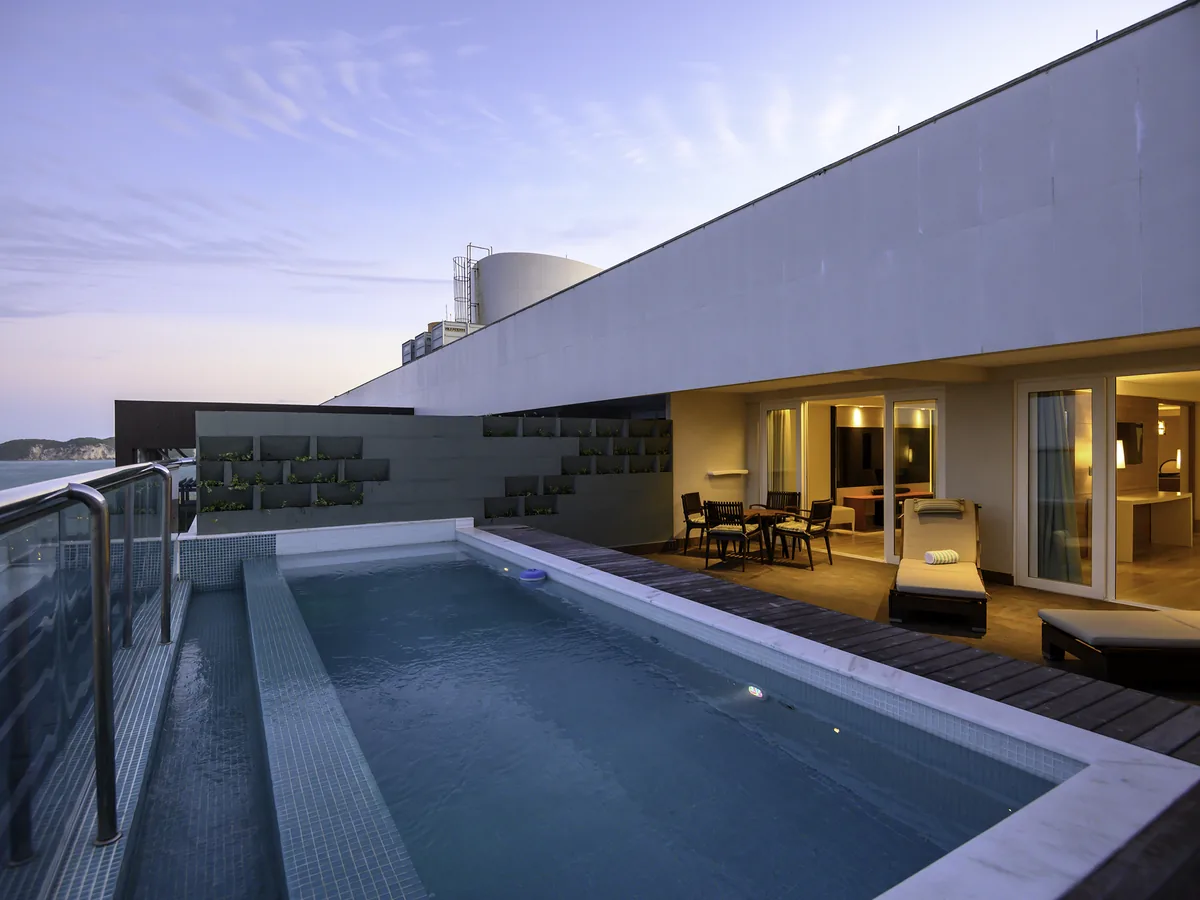 Terraço da Suíte Presidencial do Vogal ao entardecer, com piscina privativa, espreguiçadeiras e o mar à esquerda