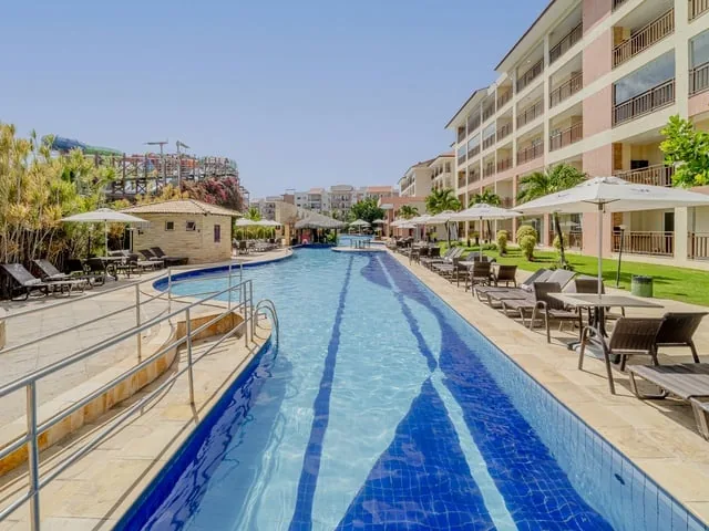 Piscina longa do Wellness Beach Park, com espreguiçadeiras, guarda-sóis e as estruturas do Aqua Park ao fundo