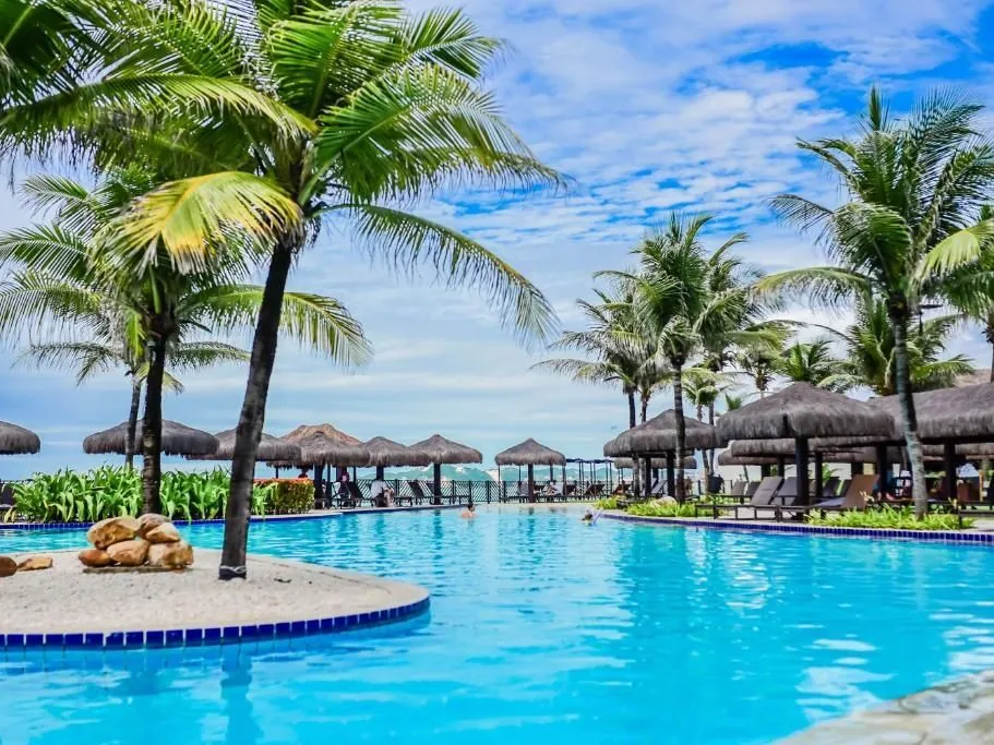 Piscina do Wish Natal Resort com coqueiros, o bar da piscina e o mar ao fundo
