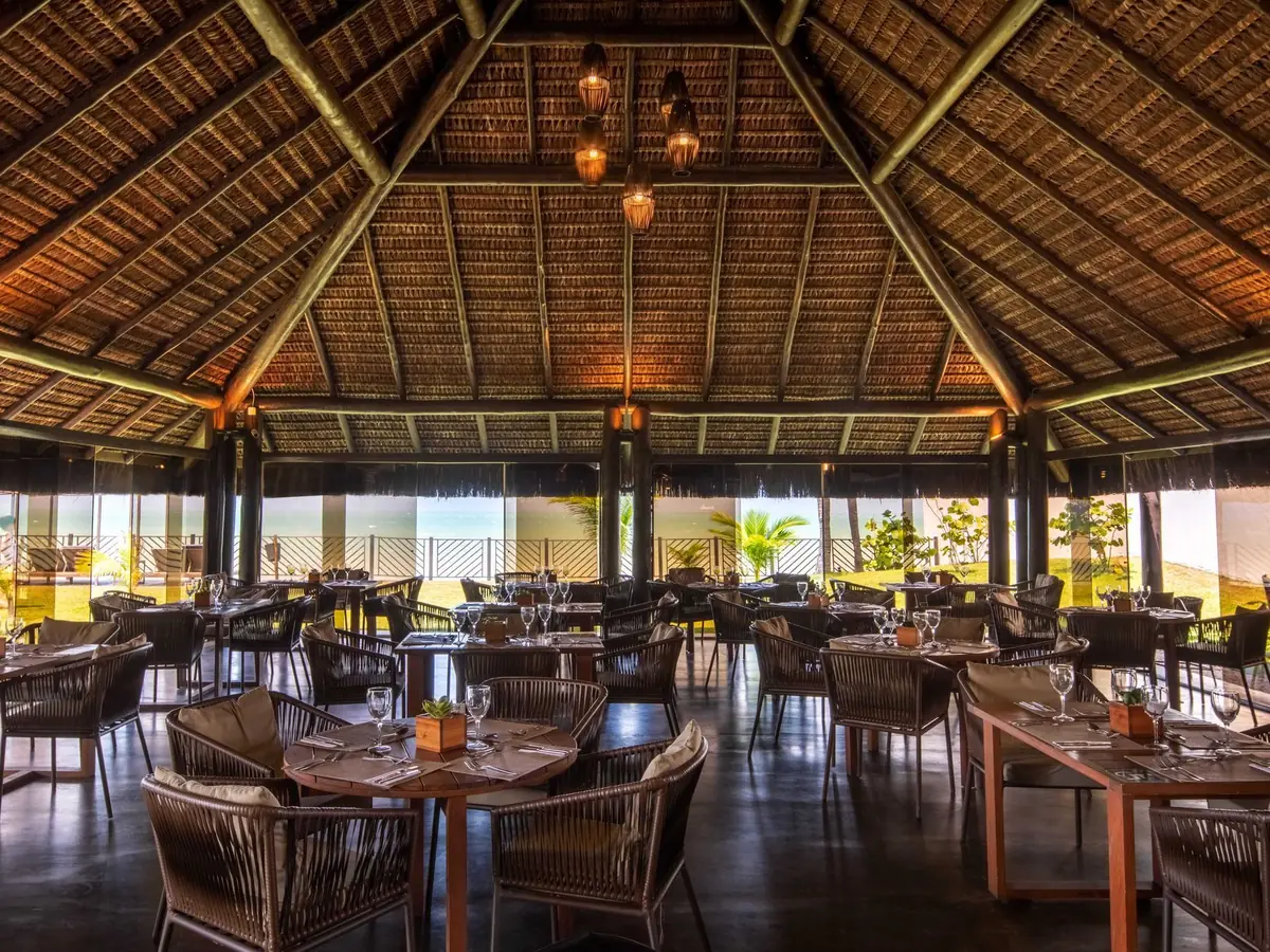 Salão de um restaurante do Wish Natal Resort, com mesas postas sob o telhado de palha