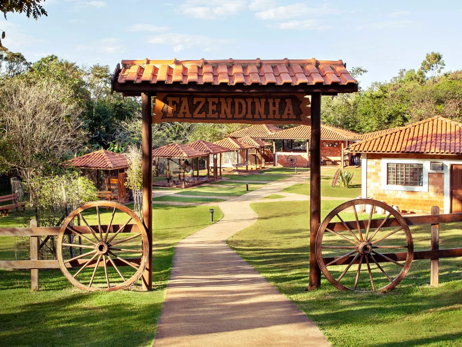Portal de madeira da Fazendinha do Aguativa, com rodas de carroça e caminho no gramado