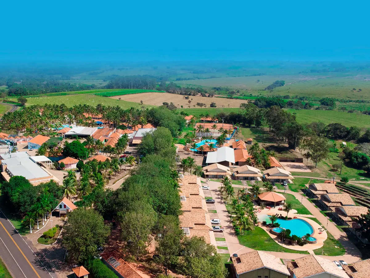 Vista aérea do Campo Belo Resort, com coqueiros, telhados, piscinas e a estrada ao lado