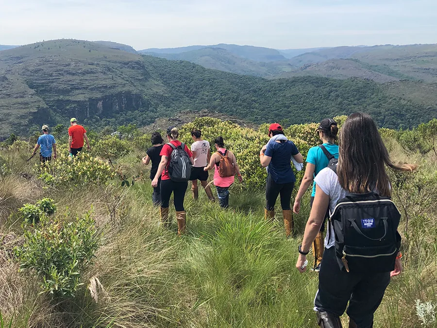 Grupo caminhando por uma trilha no campo, com o vale do cânion ao fundo