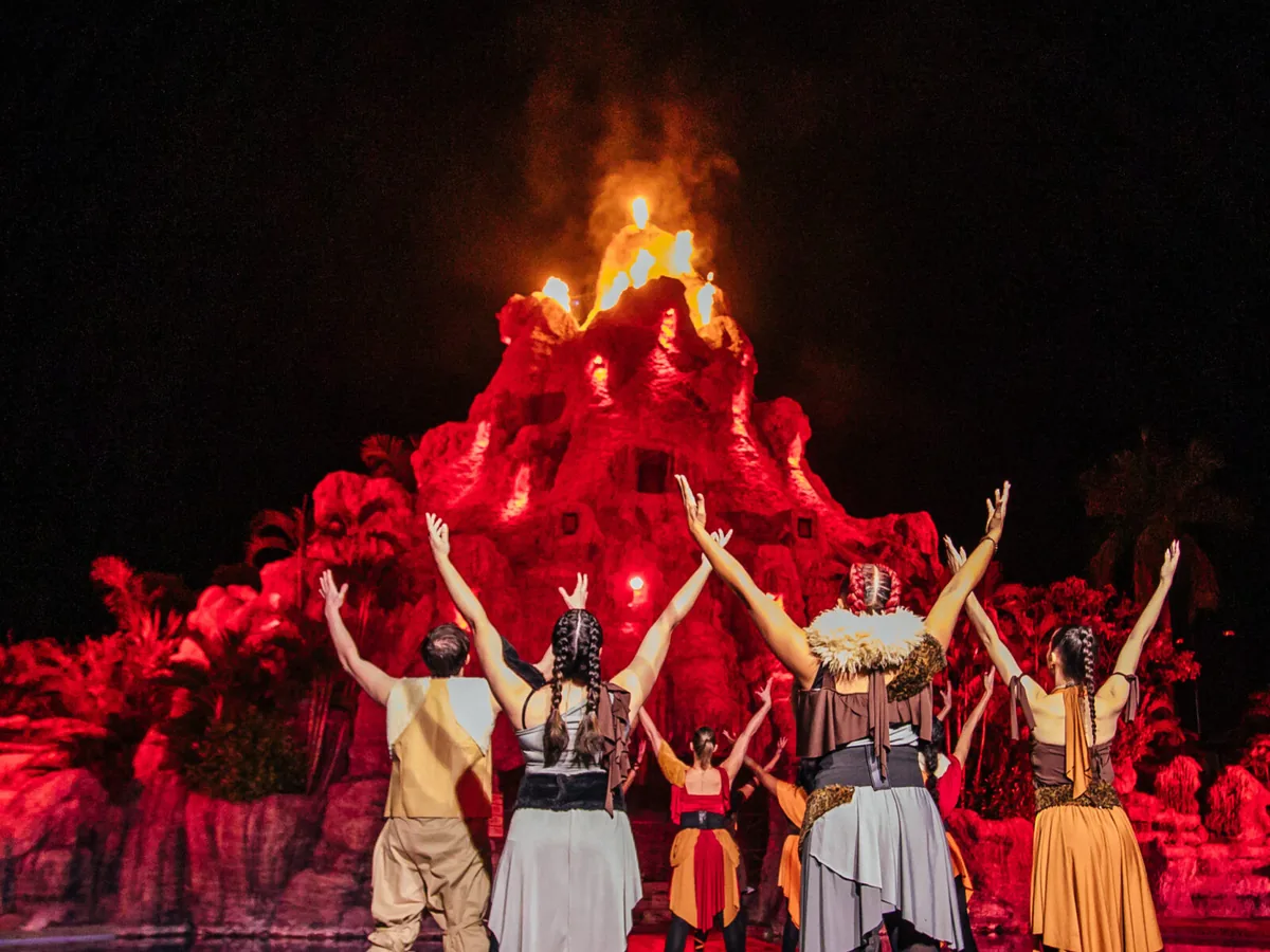 Artistas se apresentando diante do Vulcão iluminado de vermelho, com fogo no topo