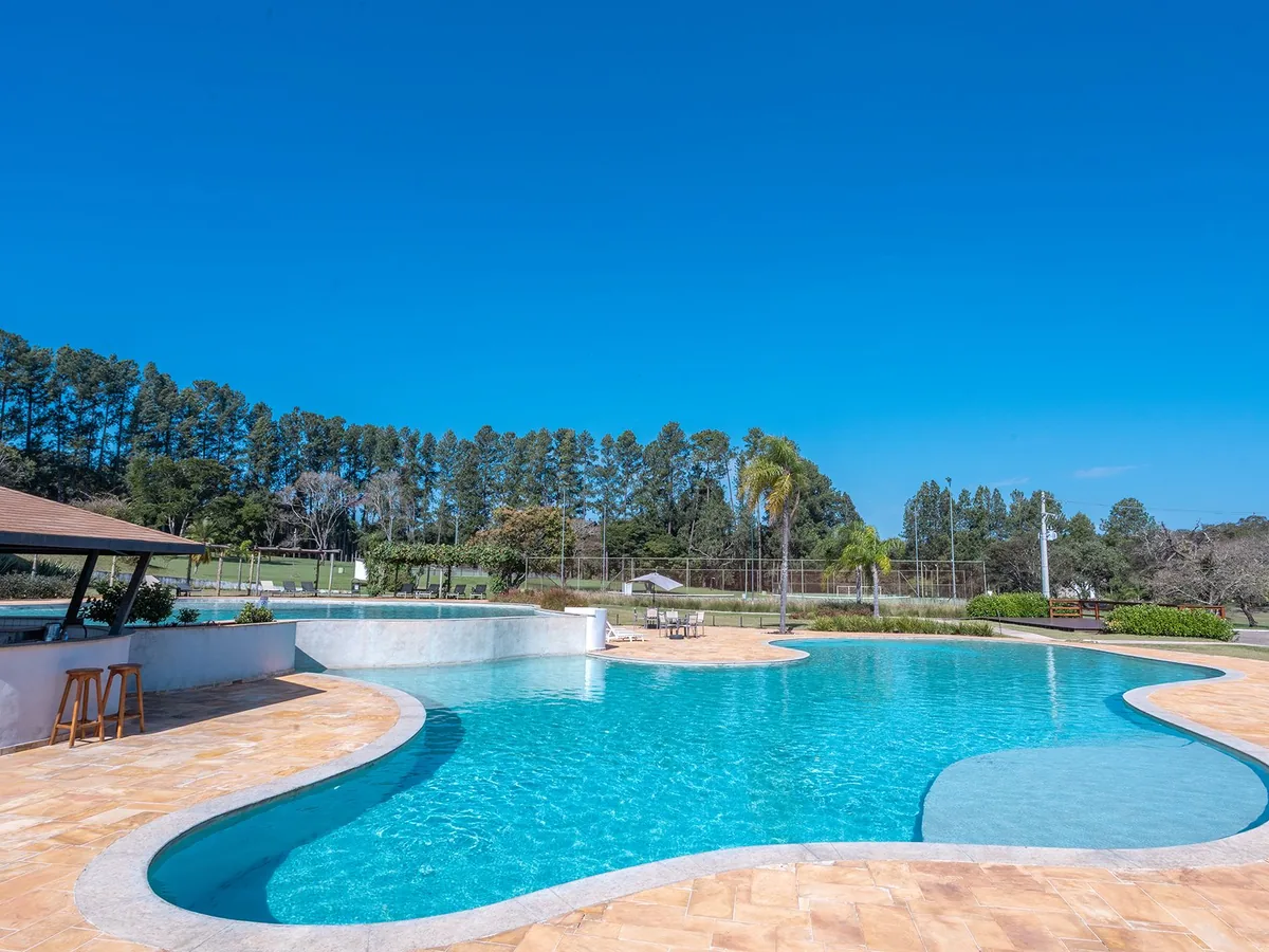 Piscina de bordas curvas do Vale das Águas sob céu azul, com pinheiros ao fundo