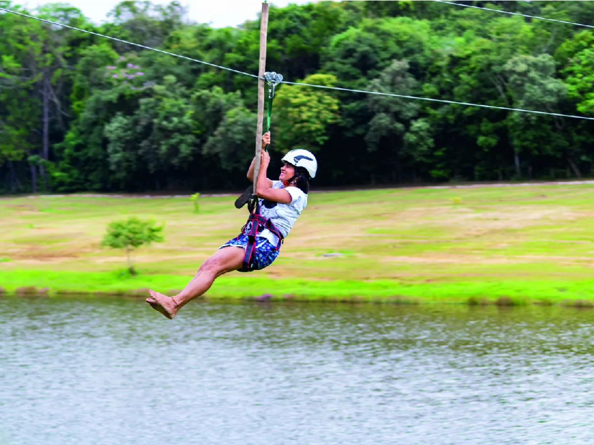 Hóspede de capacete descendo a tirolesa sobre o lago do Vale das Águas