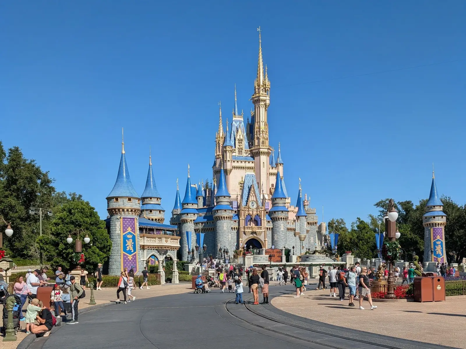 Visitantes caminhando em frente ao castelo da Disney em Orlando em dia de céu azul