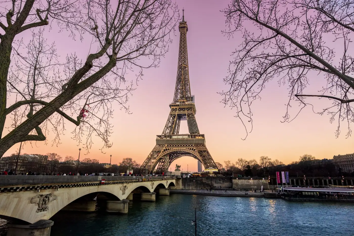 Torre Eiffel iluminada ao entardecer, vista da ponte sobre o rio Sena, em Paris