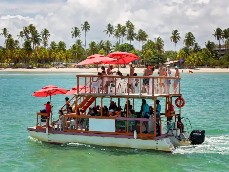 Turistas em passeio de barco com guarda-sóis vermelhos no mar verde de Porto de Galinhas